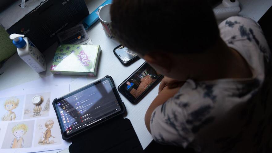 Un niño usa un móvil y una tablet, en su escritorio.